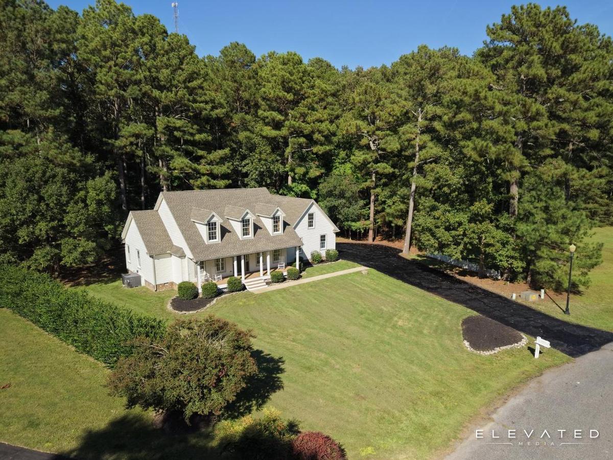 White Cape Cod home with three dormers and a front porch, set against tall pines