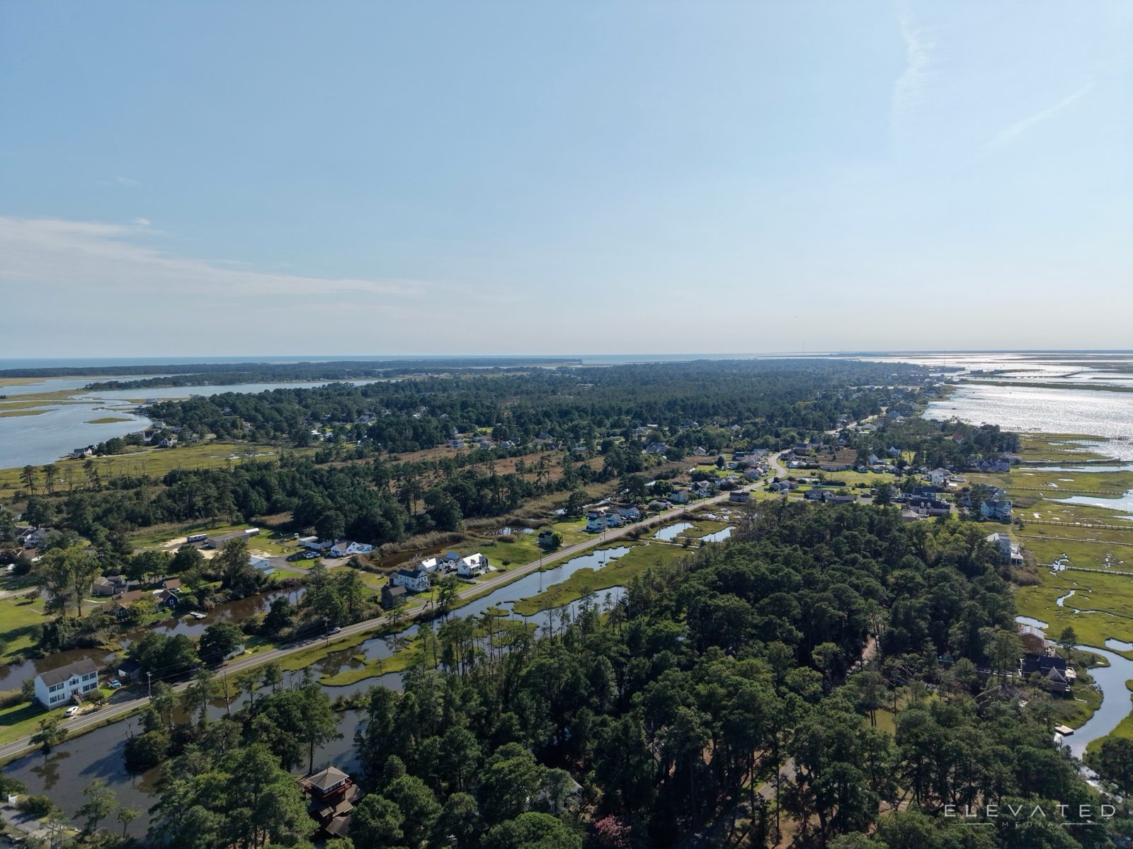Aerial of a coastal road lined with homes between salt marsh and bay