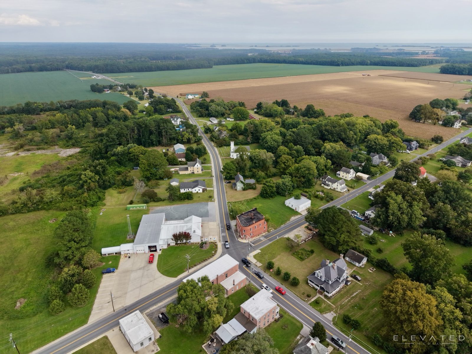 Small-town crossroads with a fire hall, church, and farm fields beyond