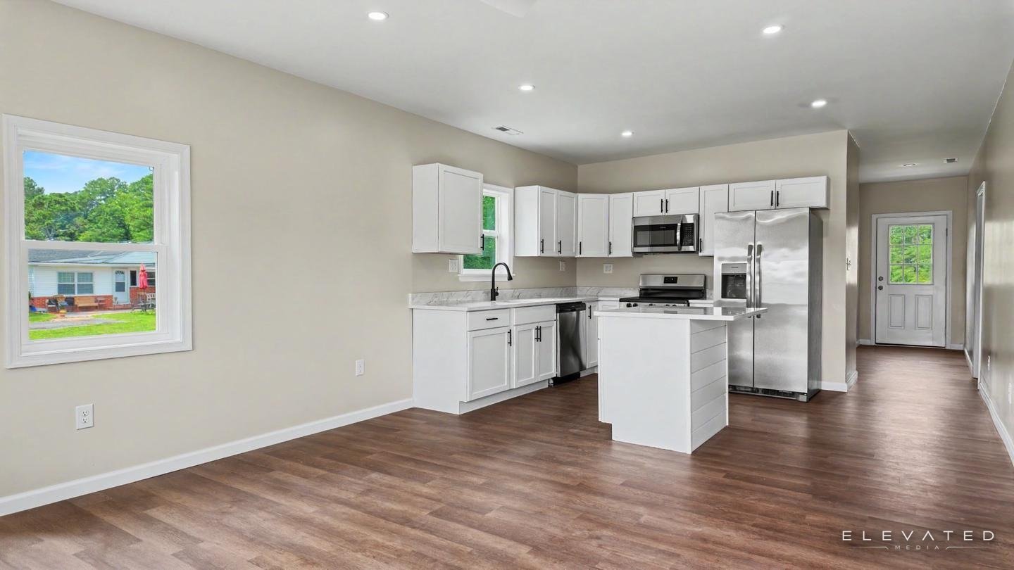 Renovated open kitchen with white shaker cabinets, stainless appliances, and a shiplap island